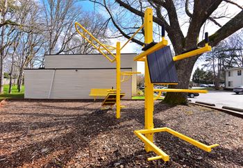 a yellow swing set in a park next to a tree
